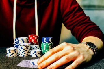 person holding playing cards beside poker chips