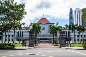 Exterior view of Singapore Parliament House with lush greenery and skyscrapers in the background.