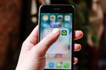 Close-up of a hand holding a smartphone displaying music apps like Spotify and Apple Music, indoors.