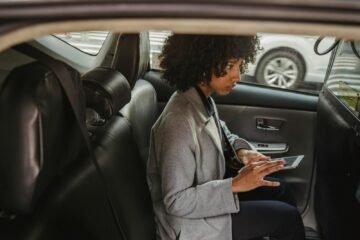 Crop black woman browsing tablet while sitting on passenger seats of taxi and looking away