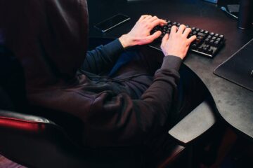 A mysterious figure in a hood typing on a keyboard, symbolizing cybersecurity threats.