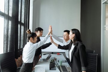 Four colleagues in a modern office high-fiving, celebrating teamwork and success.