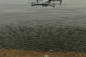 white and black drone flying over body of water during daytime
