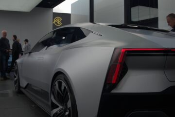 a white sports car in a showroom with people standing around