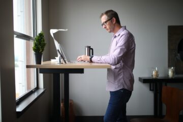 man in pink dress shirt and blue denim jeans standing beside brown wooden table