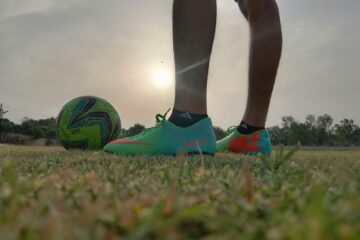 a person's legs and feet on a football ball in a field