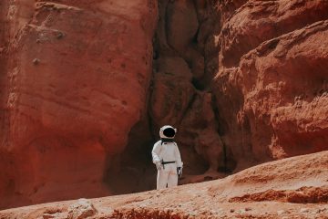 photography of astronaut standing beside rock formation during daytime