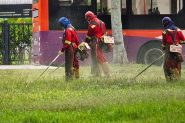 man in red jacket holding a stick near red bus during daytime