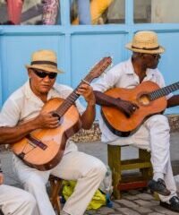 two men sitting on a bench playing guitars