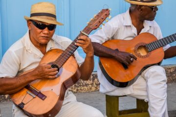 two men sitting on a bench playing guitars