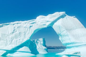 A majestic iceberg floats under the blue sky.